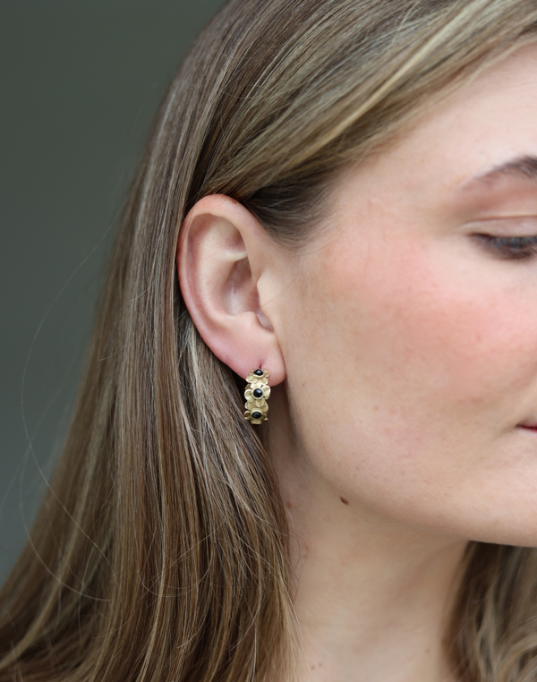 Close-up of a woman wearing gold hoop earrings with a neutral background